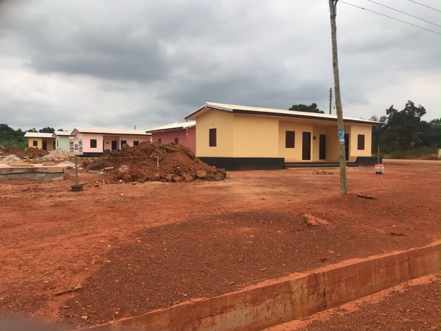 Row of newly built resettlement houses in cream, pink, and maroon at the Awonsu site, Ahafo Region, Ghana.